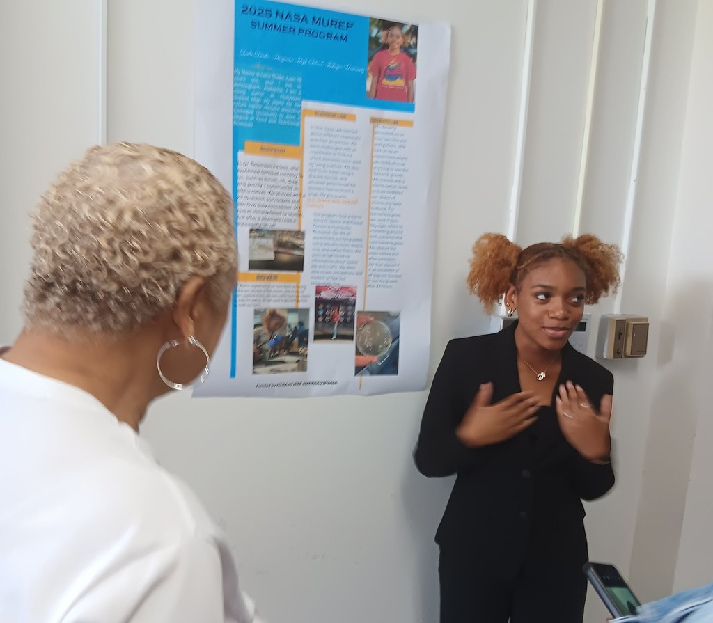 A student stands in front of a poster, giving a presentation as an adult listens