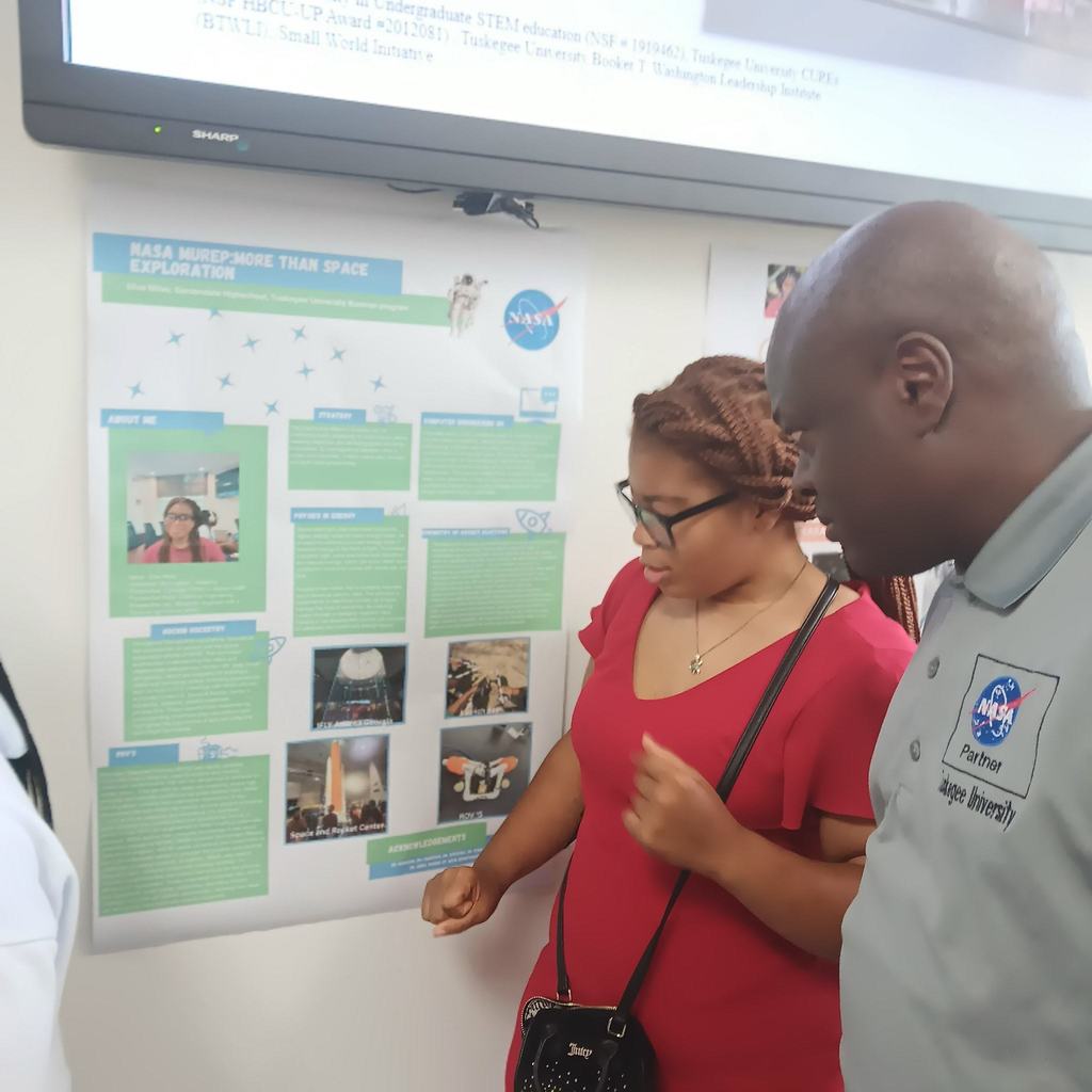 A student and adult look at a poster board placed on a wall of a classroom.