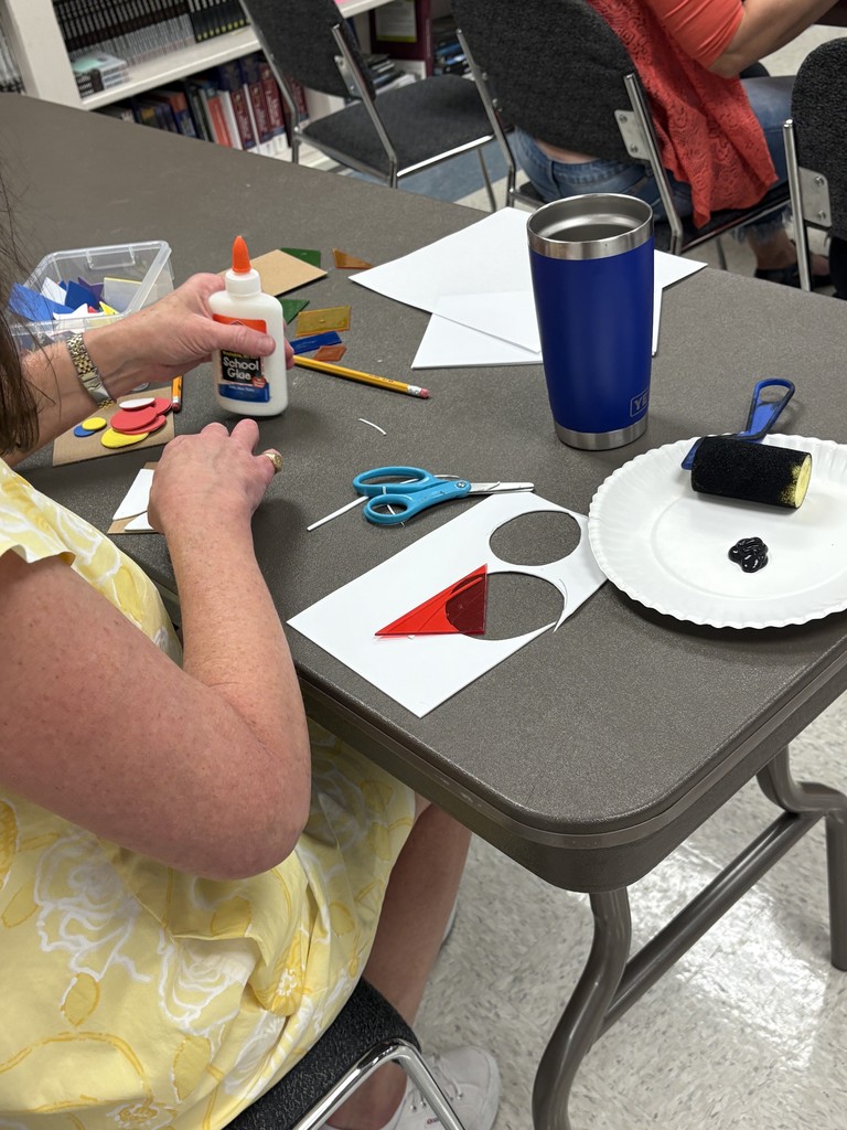 A person sits at a table with art supplies on it. The person is picking up a bottle of glue.