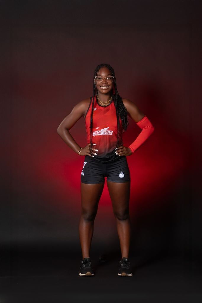 A girl wearing running clothes stands in red room and smiles at camera