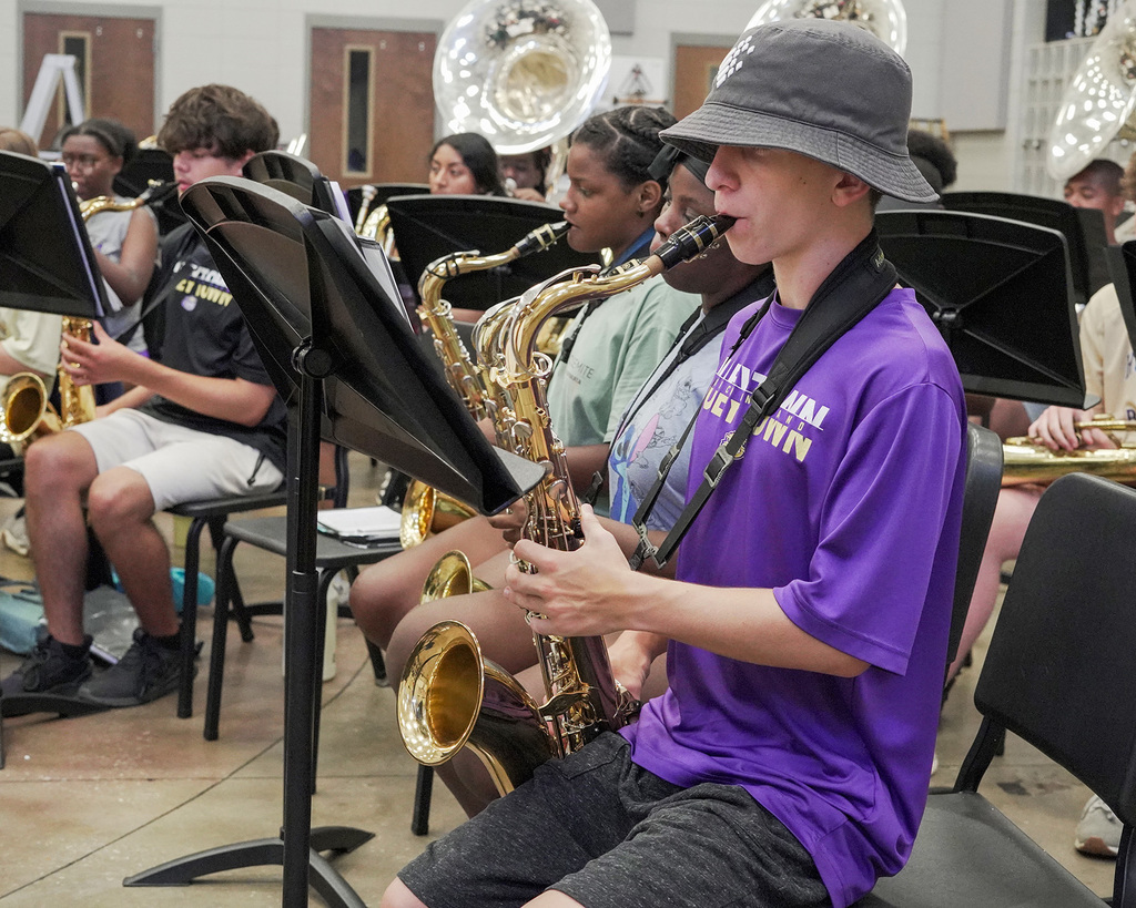 Students sit in chairs and play instruments inside a band room