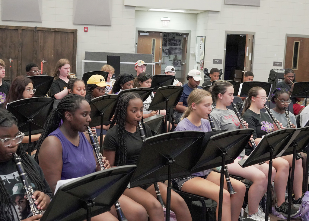 Several students sit in chairs inside band room and play instruments