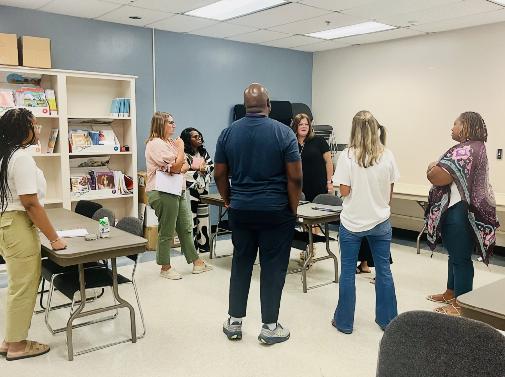 A group of adults stand and talk to each other inside a room.