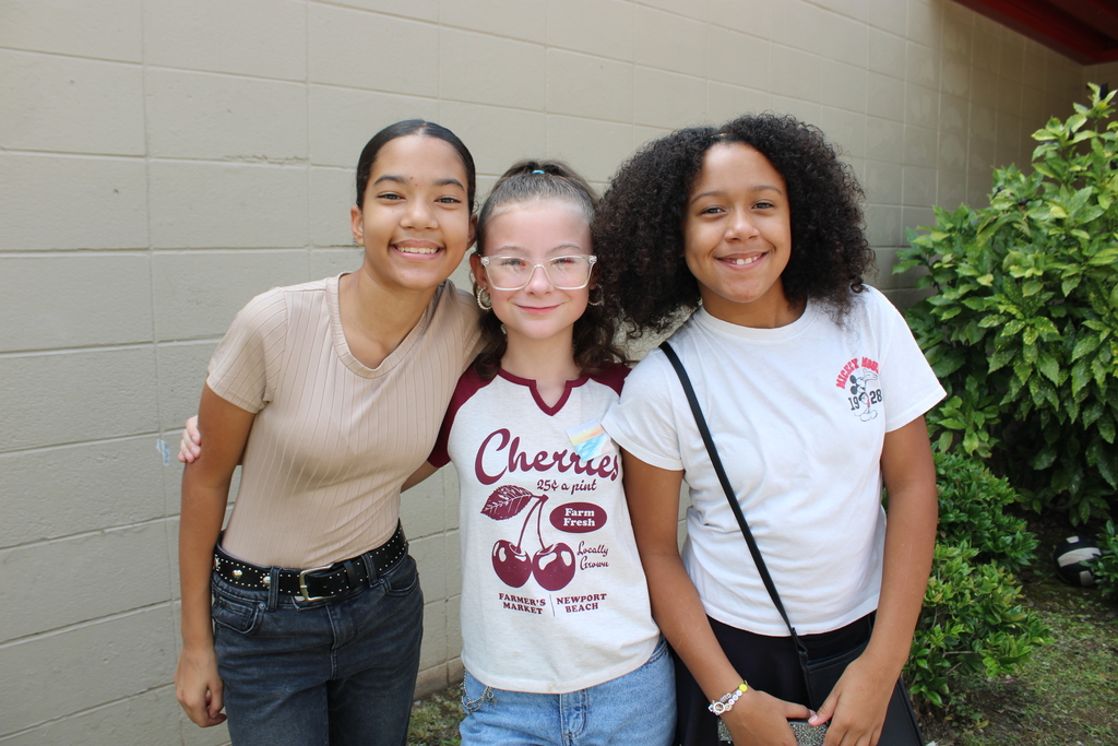 Three girls stand outside a building and smile.