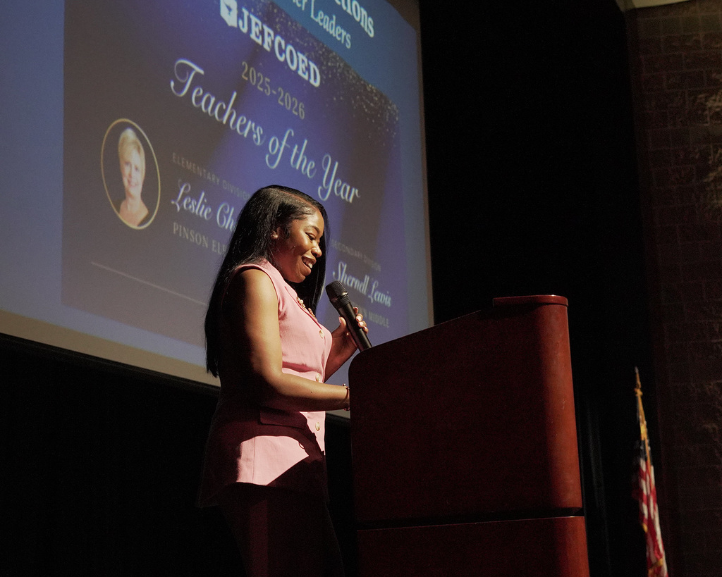 Shernell Lewis holding a microphone and presenting onstage.