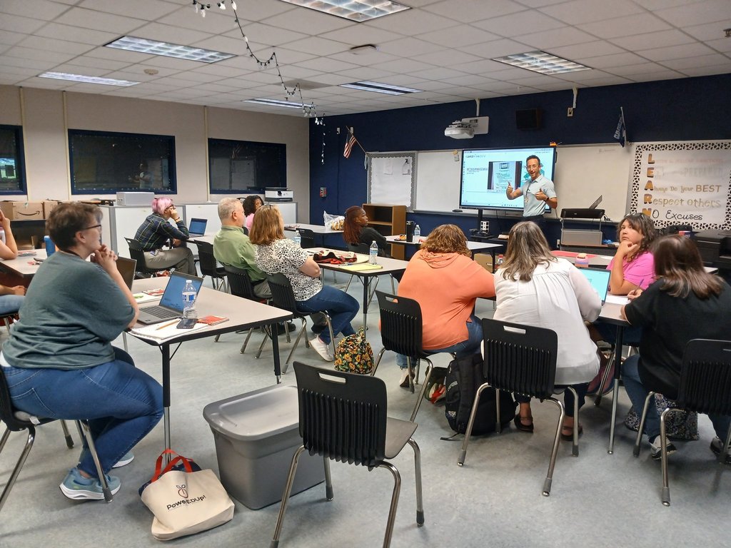 A group of people listen to a man give a presentation inside a classroom.