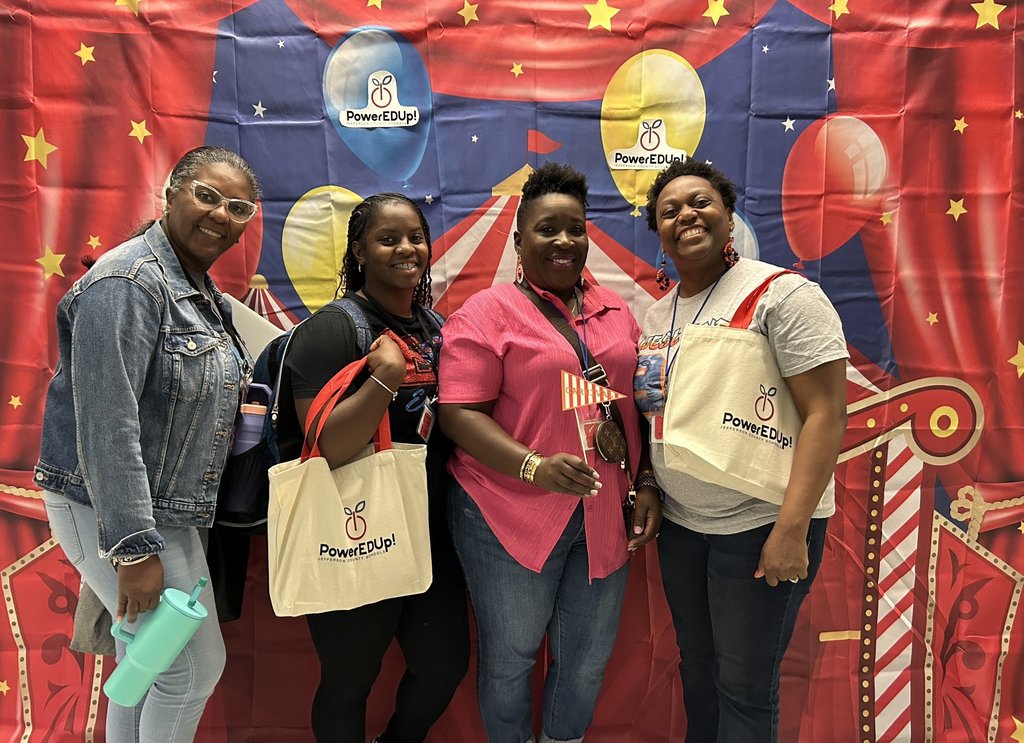 A group of women stand in front of a circus photo backdrop and smile.