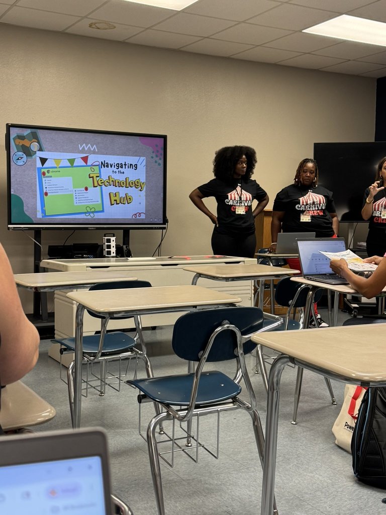 Three woman stand next to a board  in front of a classroom.
