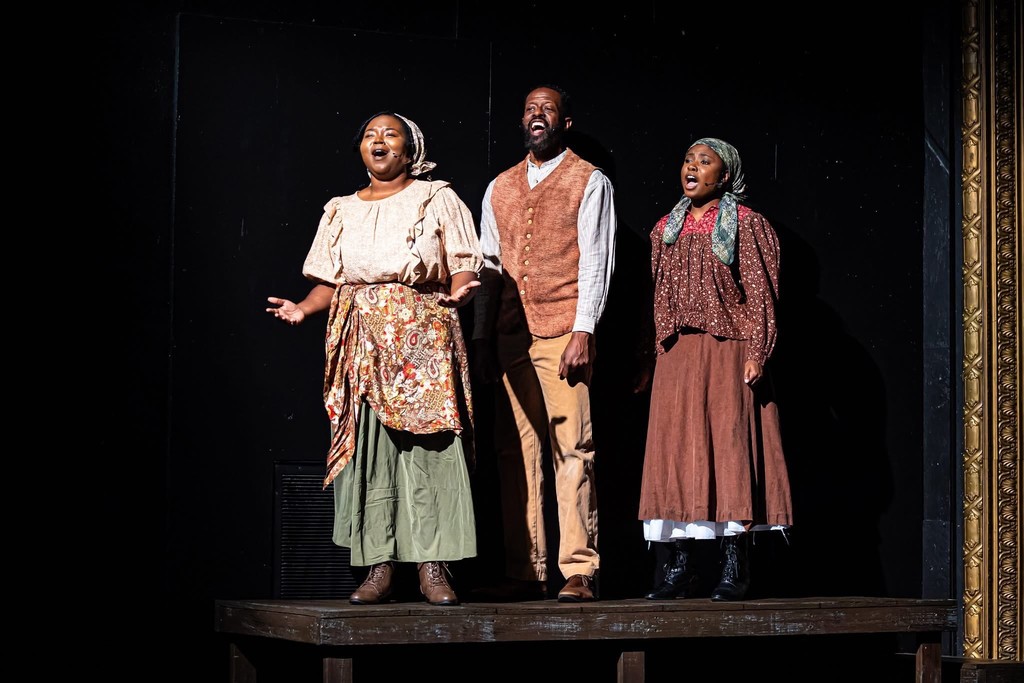 Three people stand on a stage and sing
