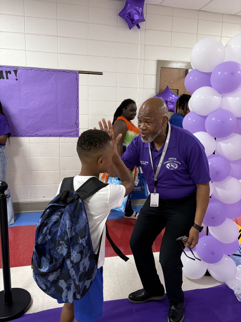 An adult stands in a school hallway and gives a high-five to a student.