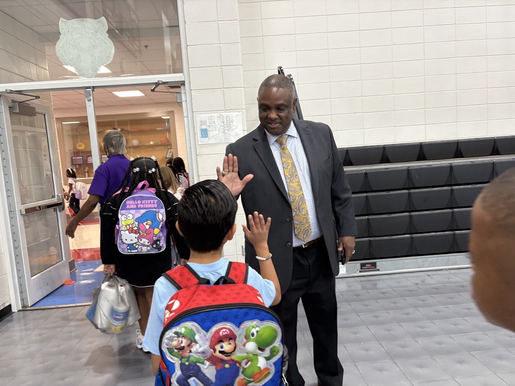 A man wearing a suit stands in a school gym and gives a student a high-five