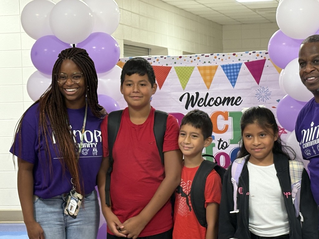 Two adults and three children pose for a picture while standing in a school hallway.