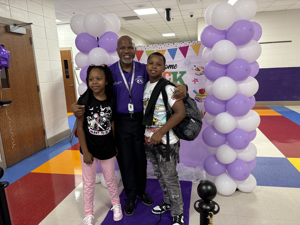 A man and two children hug and pose for a photo in a school hallway.