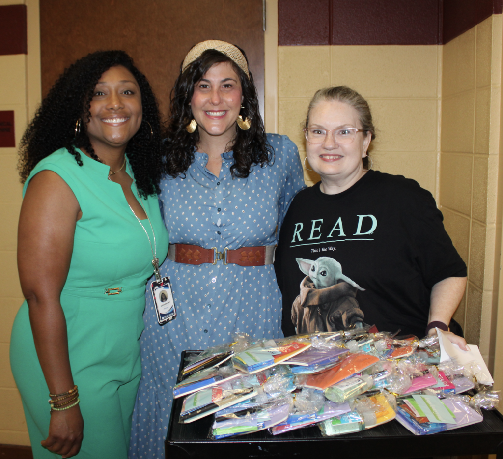 Three women stand behind a cart with goodie bags on it.