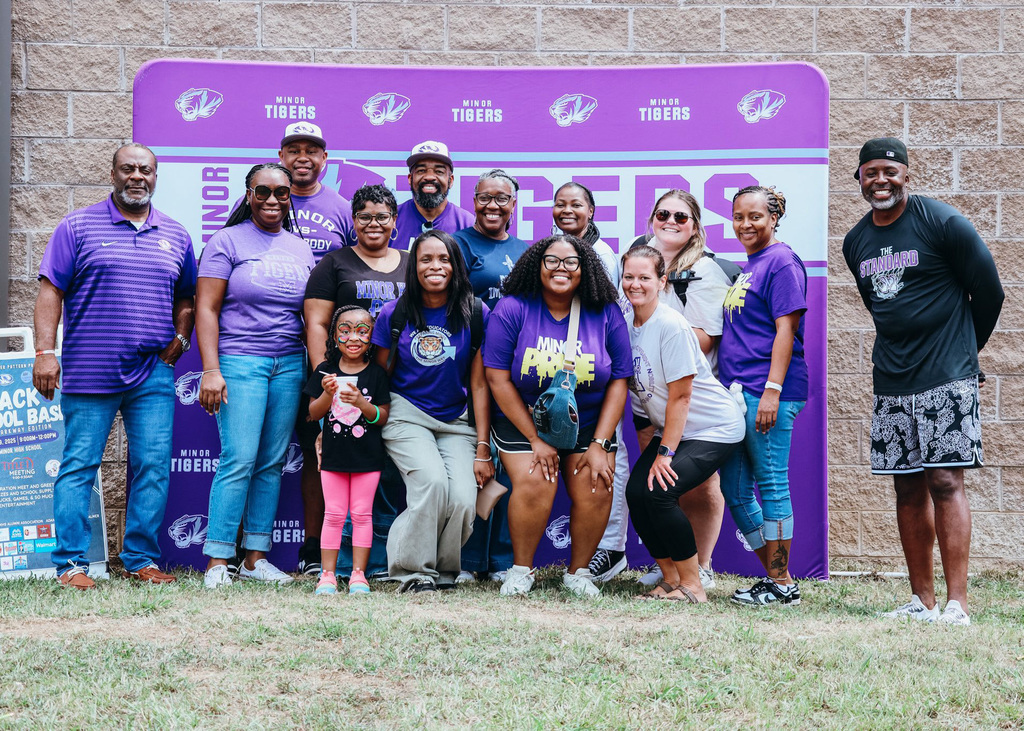 A group of adults and a child smile at the camera while standing in front of a photo backdrop set up on grass.