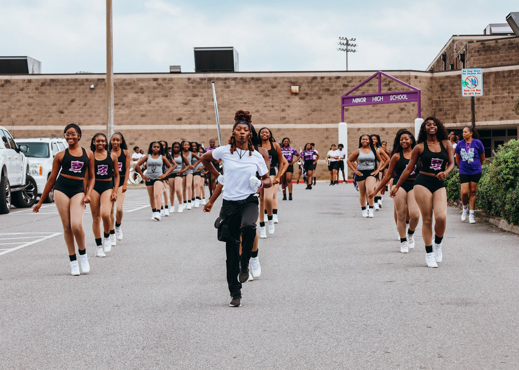 A drum major leads a marching band through a parking lot