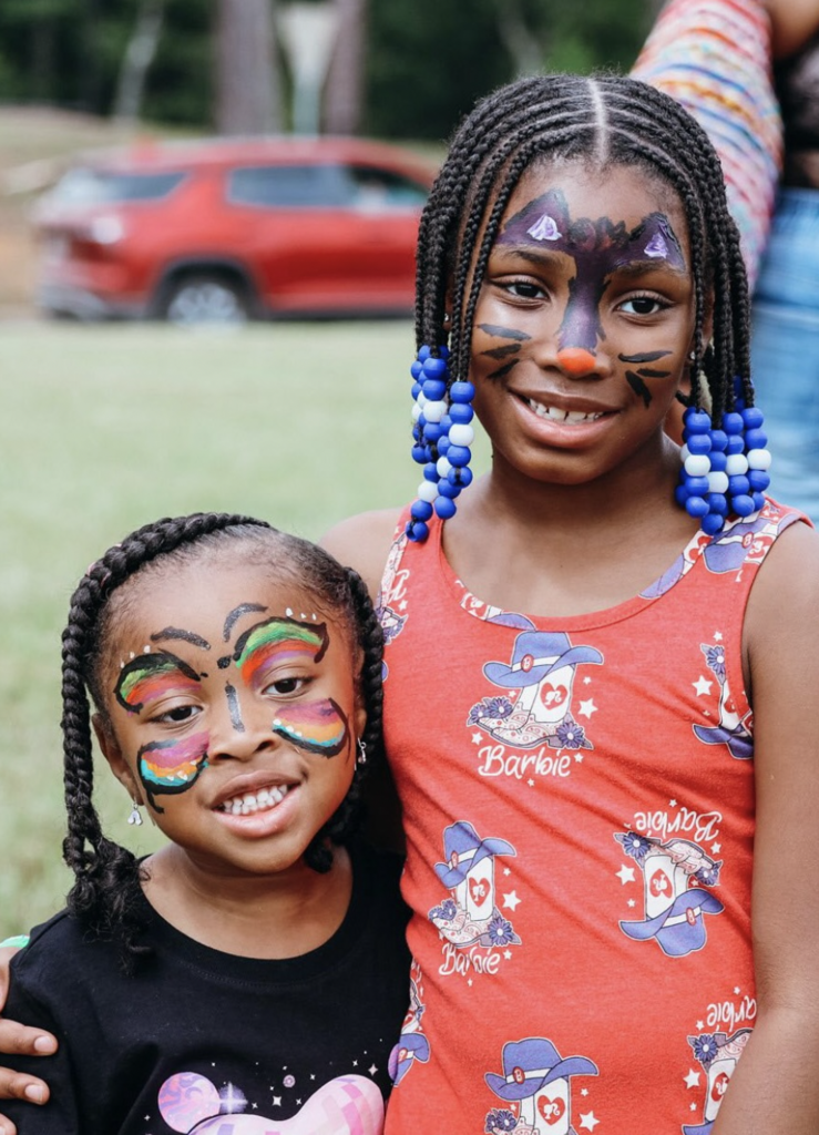 Two girls wearing face paint hug each other and smile