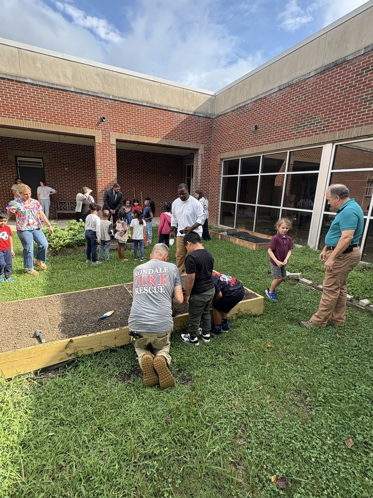 Adults and children plant seeds in a garden bed outside a school