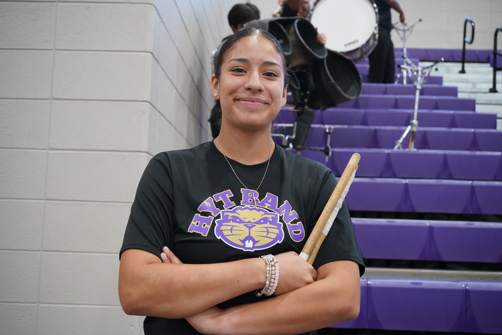 A student stands in a school gym and smiles while holding drum sticks