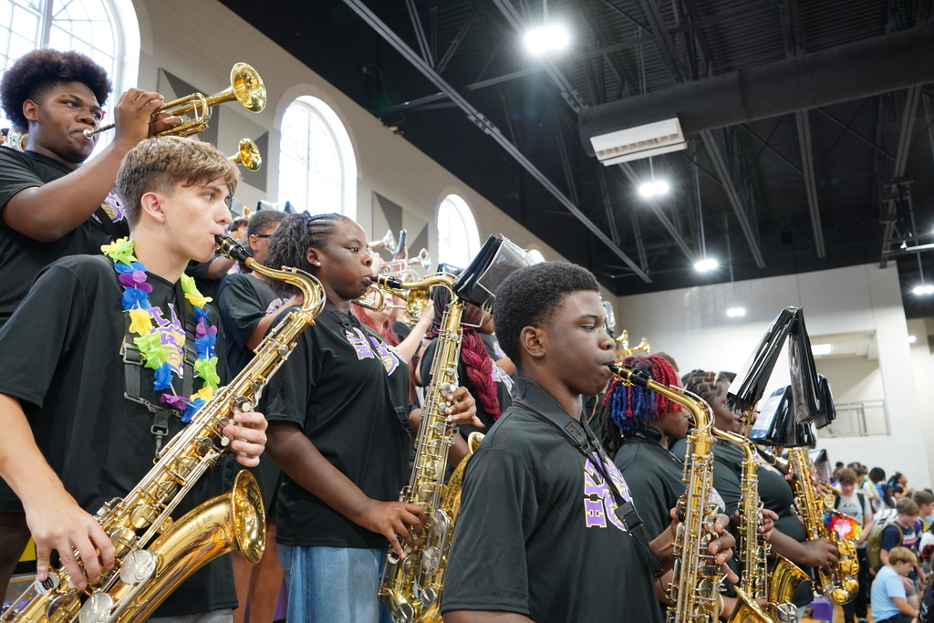 Band students stand in the bleachers at a gym and play instruments