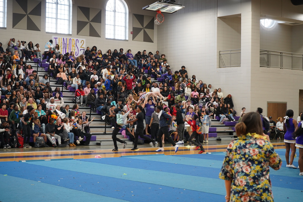 A group of students sit and stand in the bleachers of a gym.