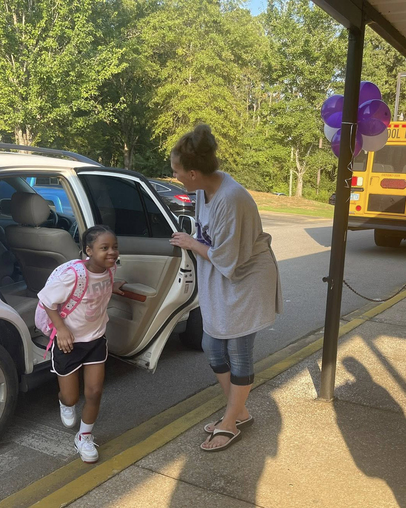 A woman helps a student get out of a vehicle in car line at school.