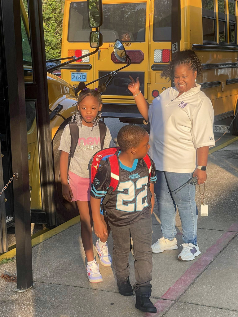 A woman greets students as they exit a school bus in the morning.