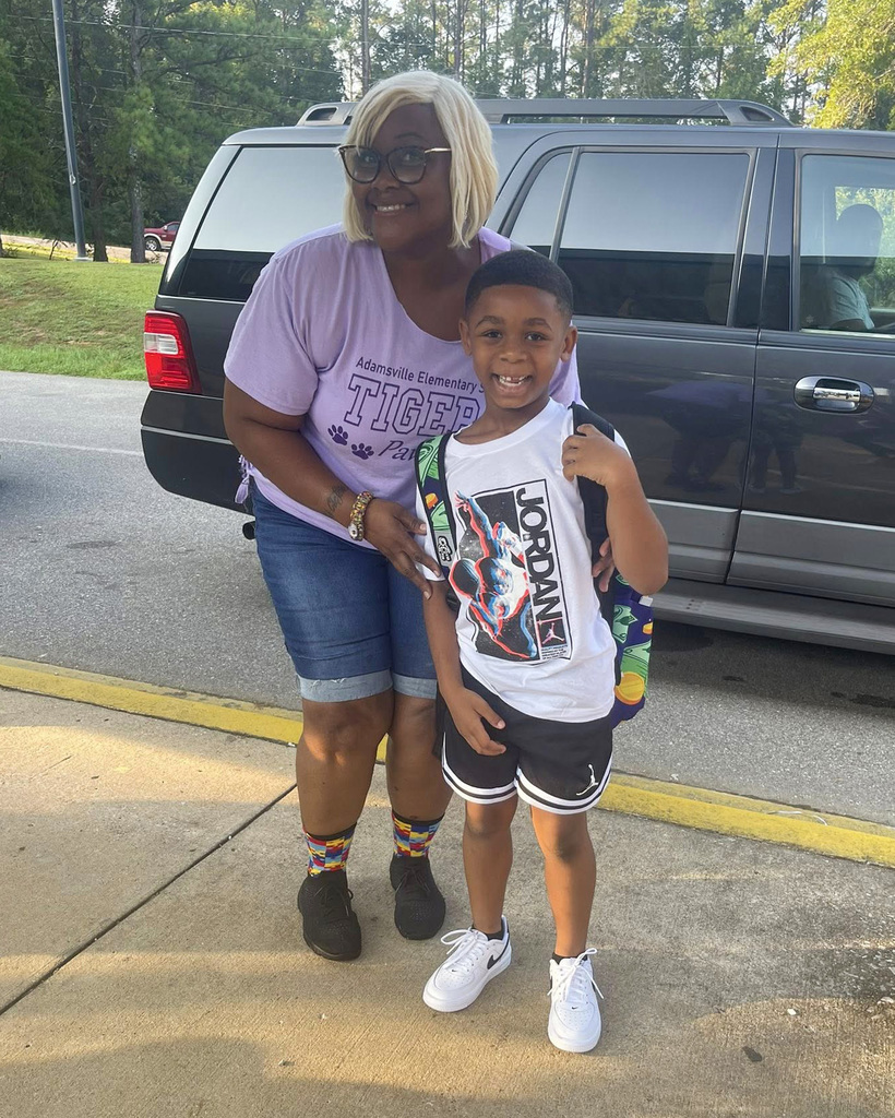 A parent and a student smile at the camera during morning car line drop off at a school.