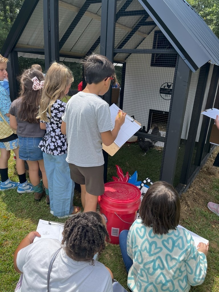 Students stand and sit outside a chicken coop.