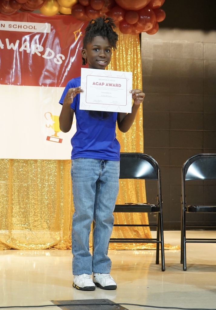 A little boy smiles while holding an award certificate