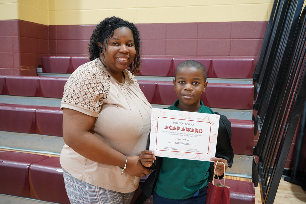 A woman and a little boy stand together and smile. The little boy holds an award