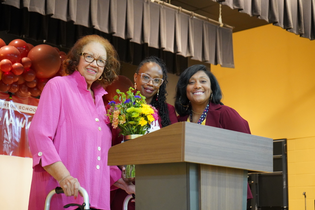 Three women stand together on a stage and smile 