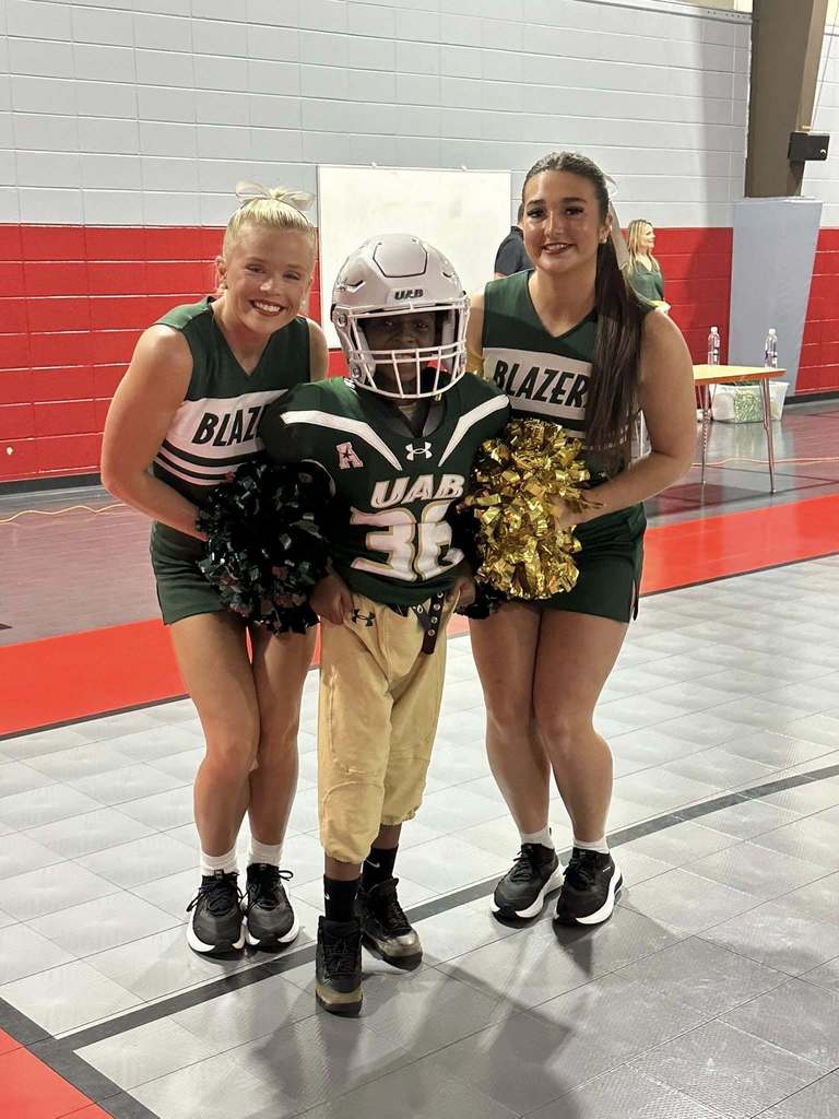 UAB cheerleaders pose with an elementary school student who is dressed in a football uniform