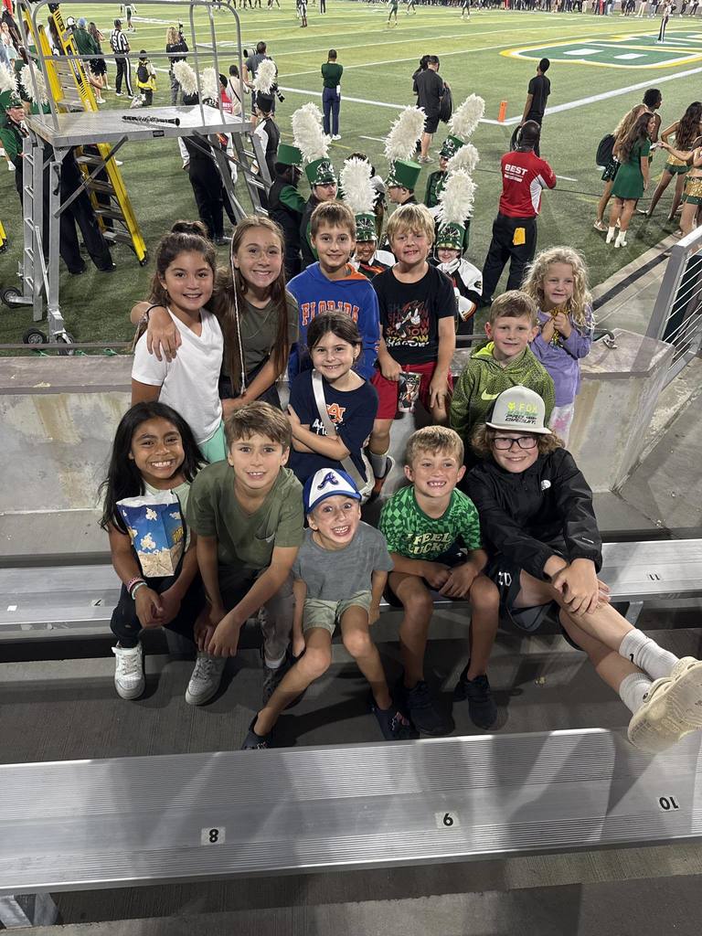 A group of students sit in bleachers at a football game and smile