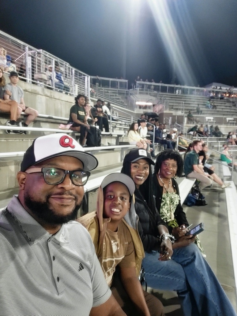 A family smiles while sitting in the bleachers at a football game