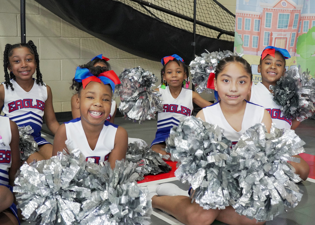 Little Eaglettes cheer members sit on the floor with pom poms.
