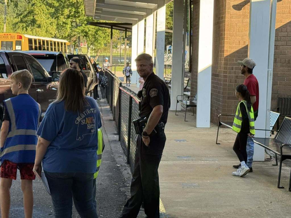 A police officer smiles toward the camera while helping with school drop-off.