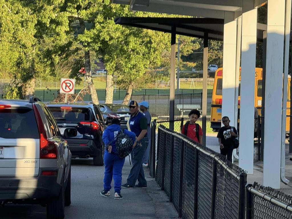 Children walk into a school while men help with carline.