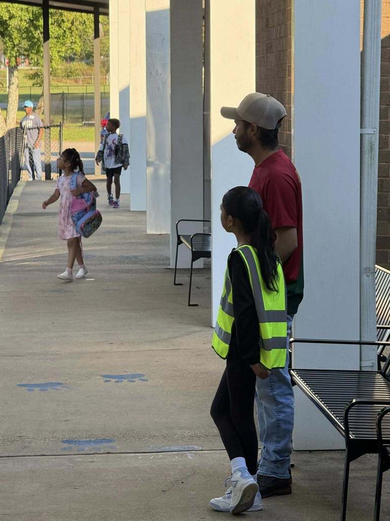A man stands next to a girl who is wearing a safety vest.