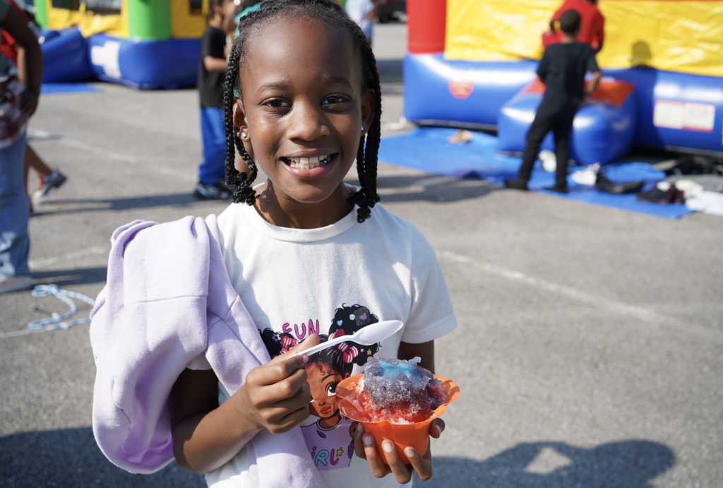 A little girl smiles while holding a snow cone.