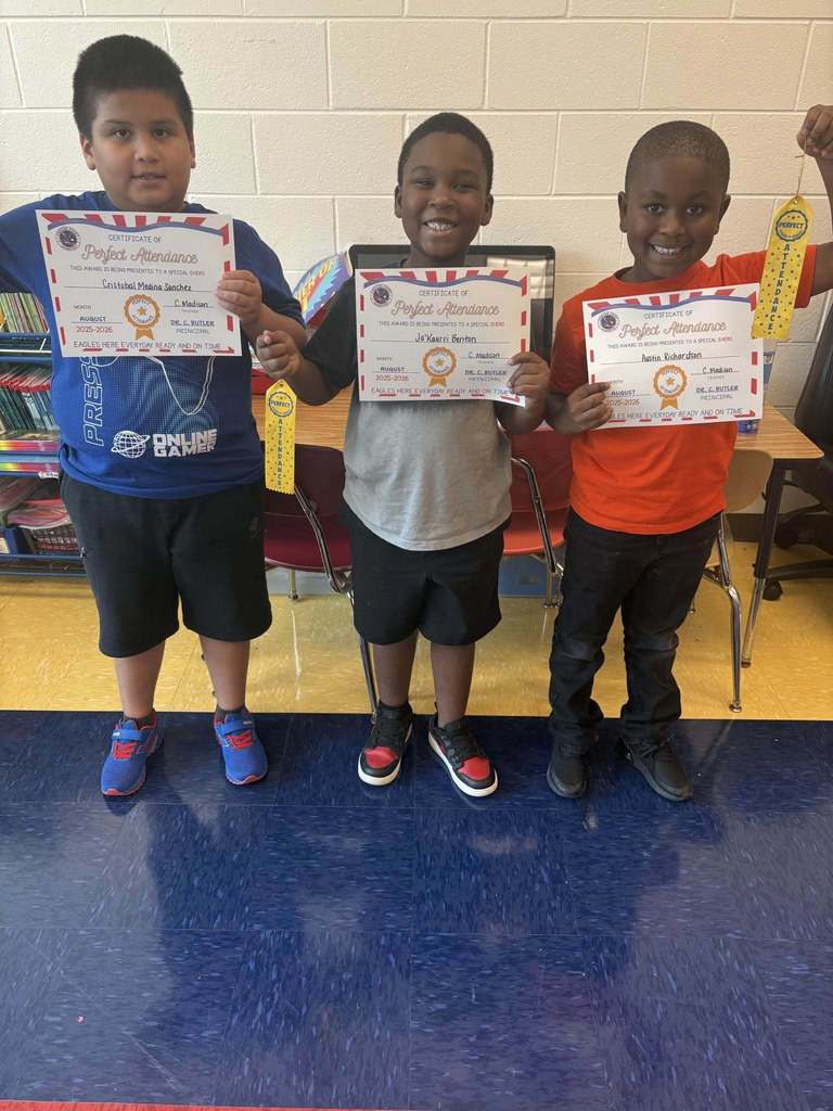 Three students stand in a school hallway, holding certificates and ribbons.