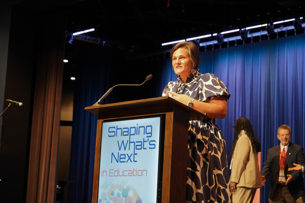 A woman stands on stage and speaks into a microphone attached to a podium. 