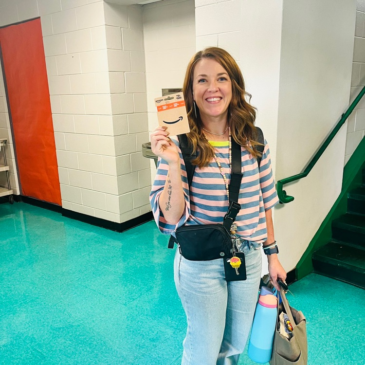 Mrs. Dillon posing for a picture holding a gift card for winning the Song of the Week.