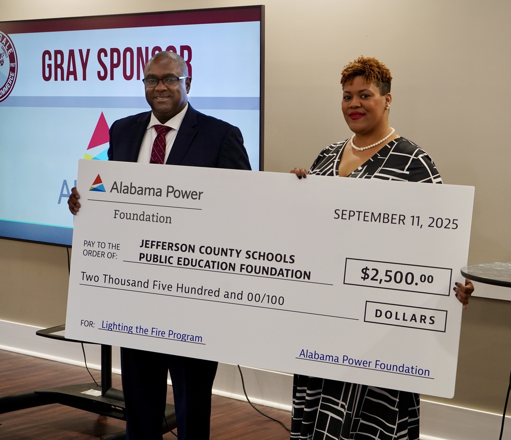 A man and a woman stand together, holding a big check and smiling.