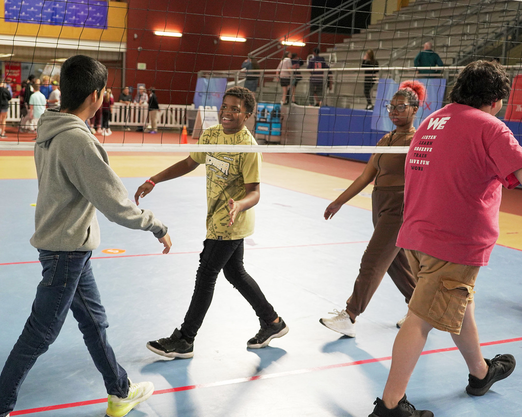 Students clap hands under a volleyball net following a game. 