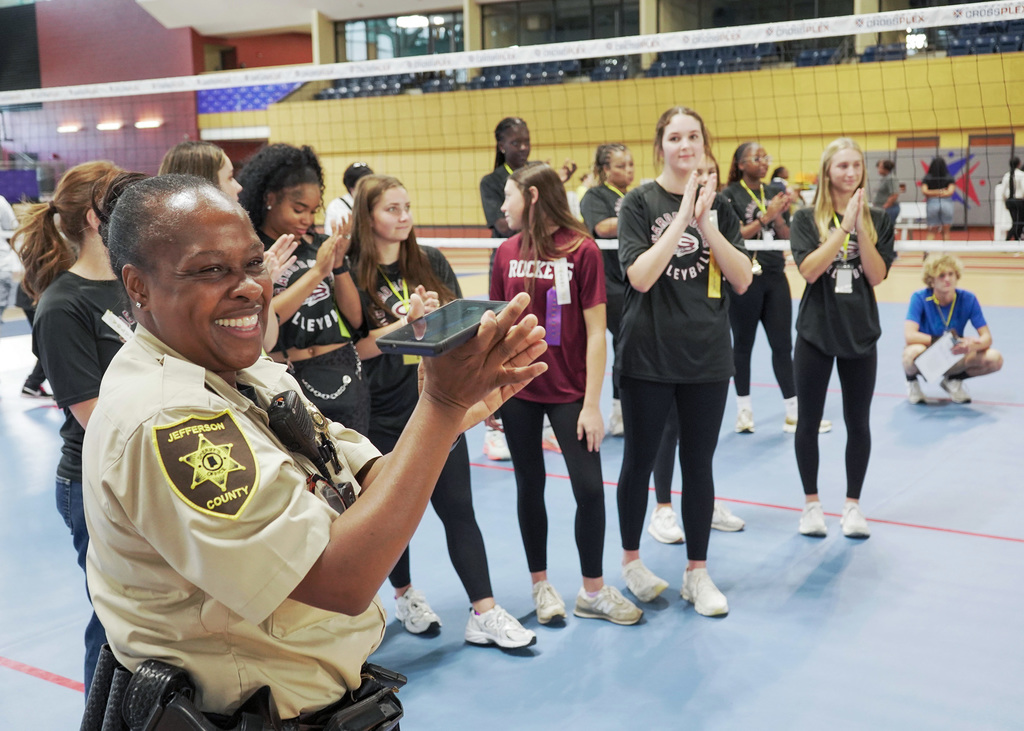 School resource officer and student volunteers clap for students during an adaptive volleyball event. 