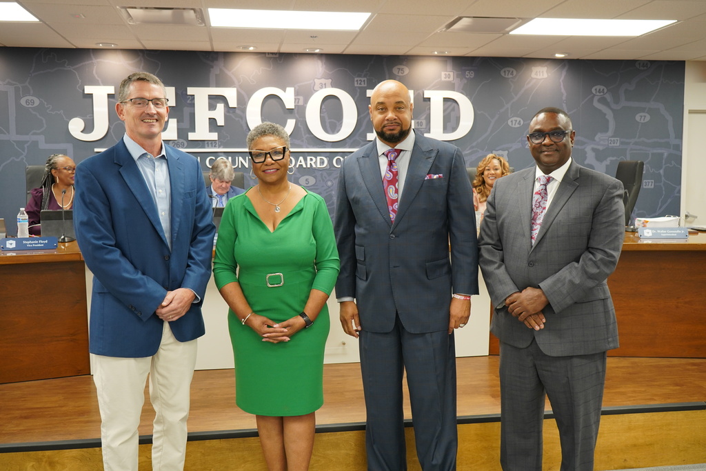 Four people dressed in nice clothes stand in a board room and smile.