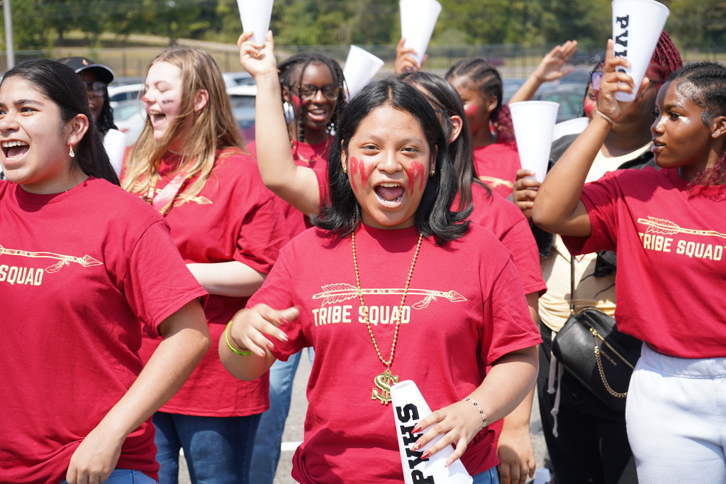 A group of students wearing red shirts that say "Tribe Squad" shout and hold megaphones.