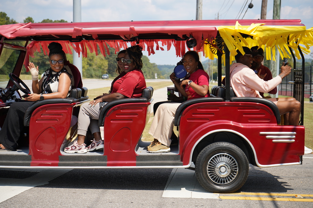 Adults smile while sitting a red golf cart on the road.