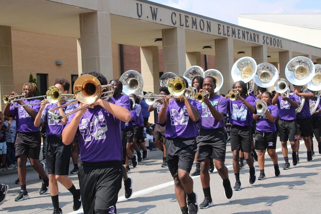Marching band members perform in front of an elementary school.